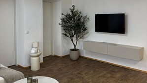 A modern living room with a round coffee table, a potted plant, a mounted TV, and a ceiling light fixture.