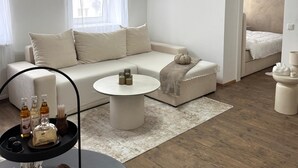 A modern living room with a beige sofa, a round coffee table, and a black side table with candles and snacks.