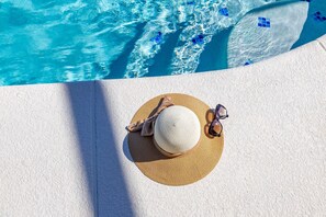 A straw hat, sunglasses, and a beach towel on a white textured surface near a pool with clear blue water. - Spacious 4BR Pool Retreat in Orange Tree – Live the Florida Life (Clermont)