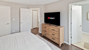 A bedroom with a bed, a TV on a wooden dresser, and two doors. - Lovely 3BR Crystal Lake home Nearby park and Lake! (Crystal Lake)