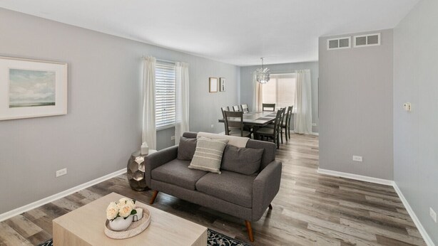 A modern living room with a gray sofa, a dining table, and a chandelier. - Lovely 3BR Crystal Lake home Nearby park and Lake! (Crystal Lake)