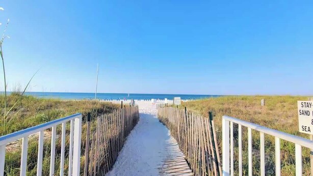 A sandy pathway leading to the beach with a sign that reads "STAY SAND & SEA."