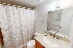 A bathroom with a toilet, sink, mirror, and shower curtain with a shell pattern. - Snowbird Rate Beachfront Complex Studio Sleeps 2! (Orange Beach)
