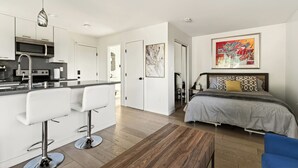 Een moderne keuken met witte barkrukken, een bed met gestreepte kussens en een groot abstract schilderij aan de muur.