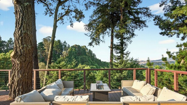 Een terras met tuinmeubilair, waaronder een bank en stoelen, omringd door bomen en een balustrade.