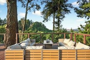 Une terrasse dotée de mobilier d’extérieur, comprenant un canapé et des fauteuils, entourée d’arbres et agrémentée d’une rambarde.