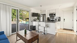 Een moderne keuken met witte kasten, een roestvrijstalen koelkast en een magnetron. Er is een bar met twee witte barkrukken.