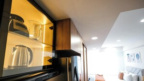A modern kitchen with a built-in refrigerator, a glass-fronted cabinet displaying kitchenware, and a view into a living area with a sofa and artwork on the wall. - Tribeca Park by Jalo (Bogotá)