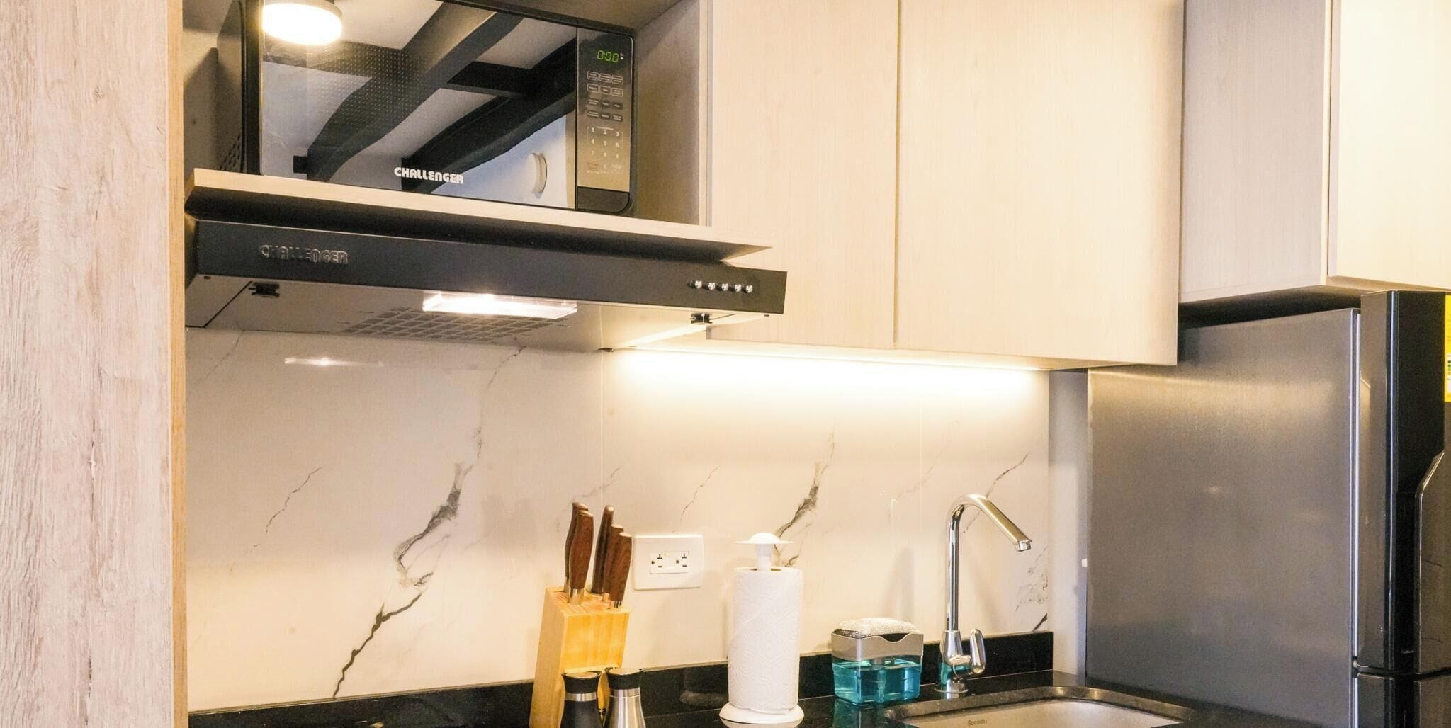Una cucina moderna con forno a microonde integrato, frigorifero in acciaio inossidabile e una parete di fondo in marmo.