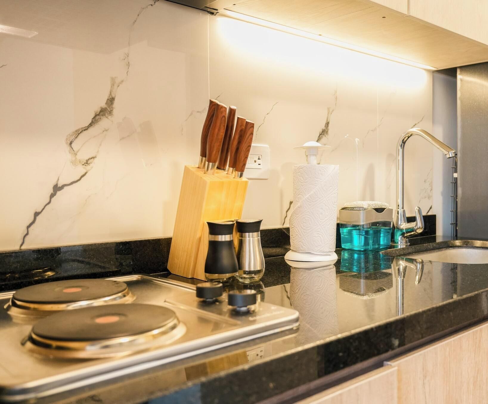 Una cocina con salpicadero de mármol, un fregadero, una cafetera y un bloque de cuchillos.