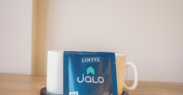 Eine weiße Tasse zusammen mit einem Kaffeepäckchen mit den Aufschriften 'COFFEE' und 'JALO' auf einem Untersetzer.