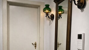 Um corredor com uma porta branca, um espelho grande e um termostato fixado na parede.