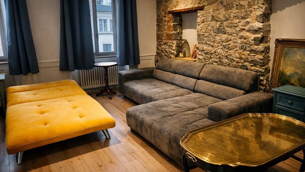 Uma sala de estar aconchegante com uma parede de pedra, um sofá, um banquinho amarelo e uma mesa de centro de vidro.