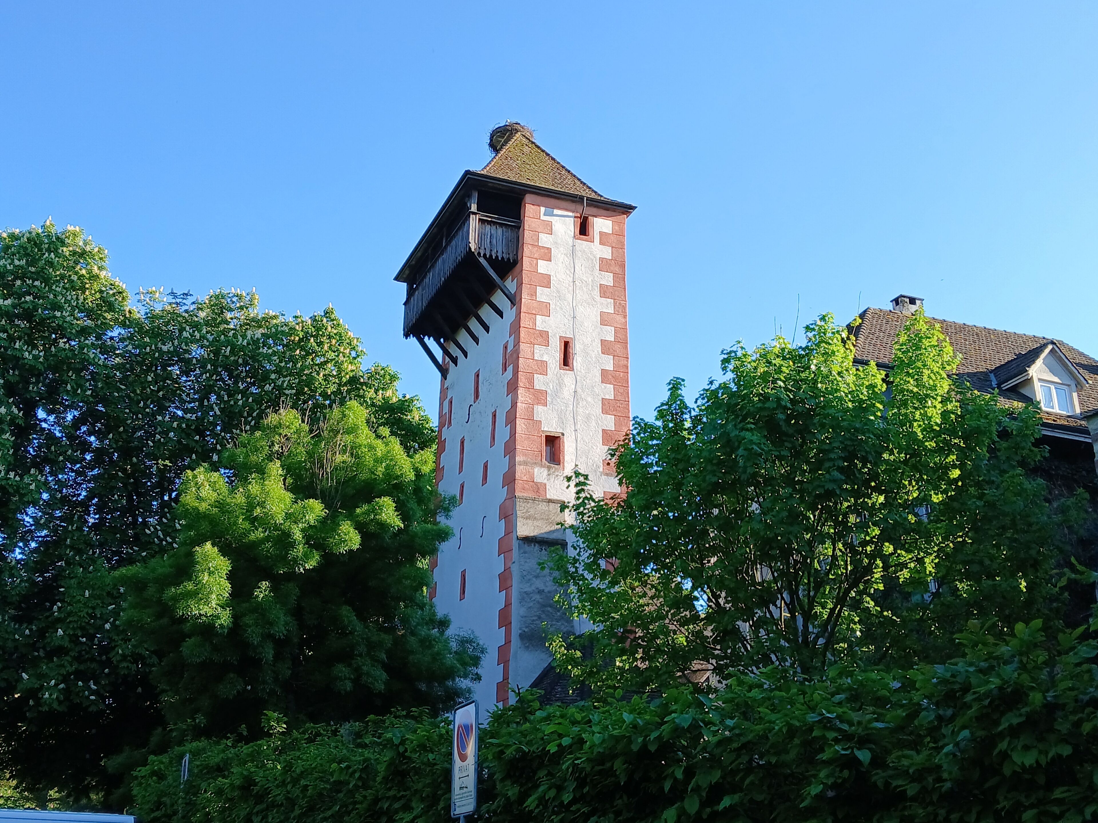Ein historischer Turm mit Backsteinfassade und einem Balkon, umgeben von üppiger Vegetation.
