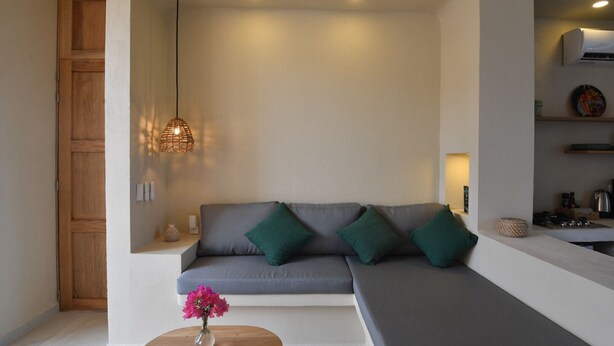 A modern living room with a grey sofa, green cushions, a small wooden table with a vase, and a hanging light fixture. - Taormina Starlink House -10 guests, AC, Safe Neighborhood (La Barra de Colotepec)
