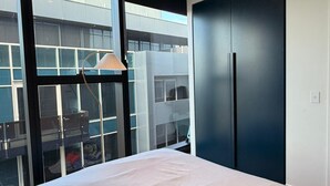 Un dormitorio moderno con una cama grande, un armario y vistas de un edificio a través de un amplio ventanal.
