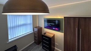 A modern room with a large ceiling lamp, a flat-screen TV mounted on the wall, and built-in wooden cabinets. - Modern Spacious 2-Bed Apartment • Sleeps 4 • Near City Centre free parking (Manchester)