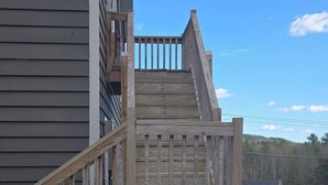 A wooden staircase leading to a deck, a gray building, and a clear sky with clouds.