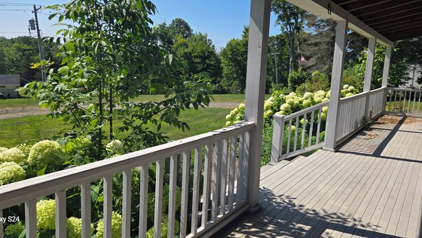 A covered porch with a wooden deck and white railings.