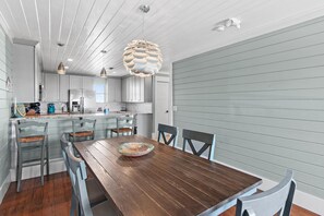 A modern kitchen with white cabinets, a wooden dining table, and a unique pendant light. - Costa Vista Townhouse #13 (Miramar Beach)