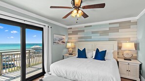 A bedroom with a large bed, two bedside tables with lamps, a ceiling fan, and a view of the ocean through a sliding door. - Costa Vista Townhouse #13 (Miramar Beach)