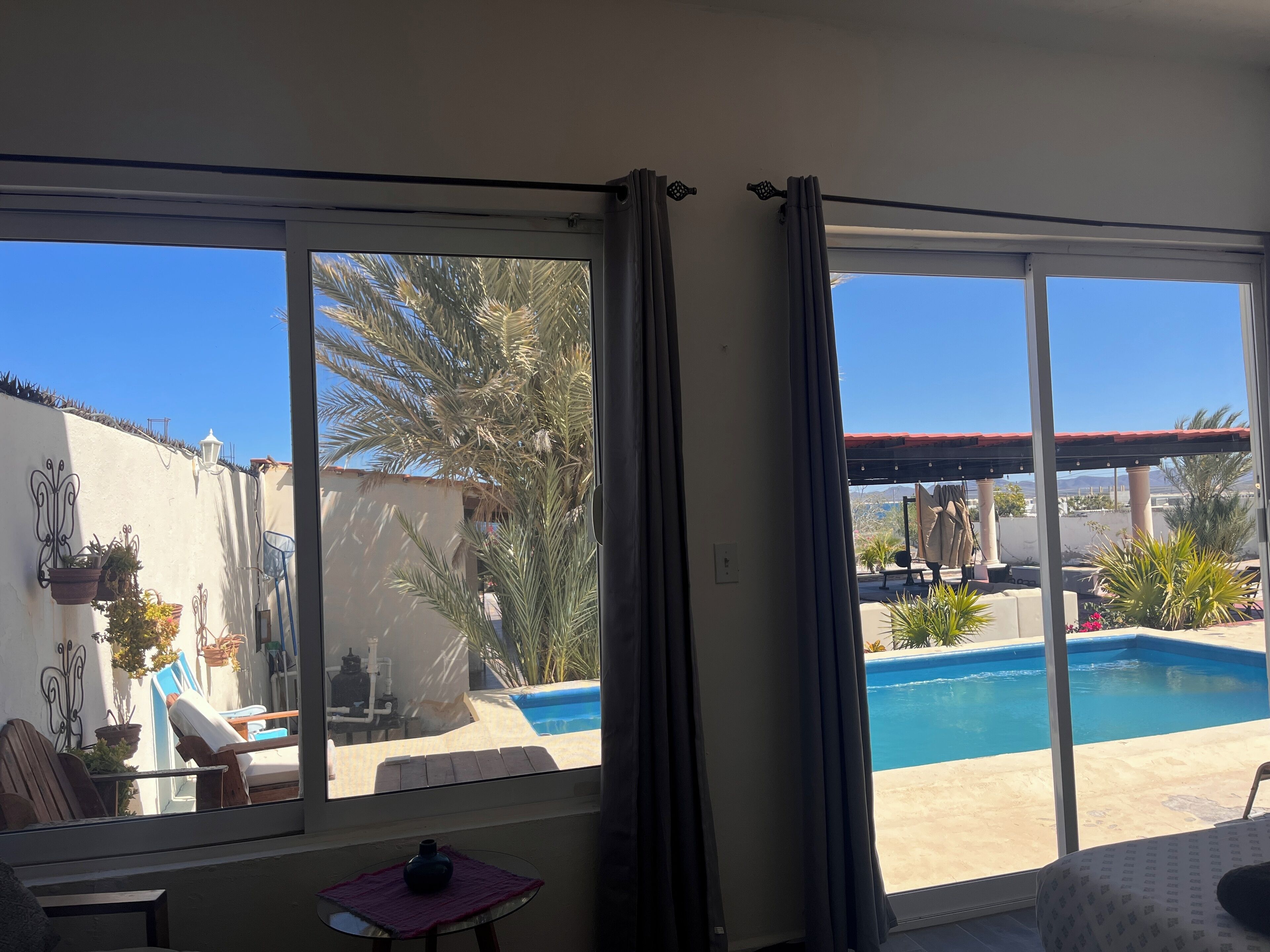 A room with a large sliding glass door leading to a pool area, a small table with a vase, and a chair.