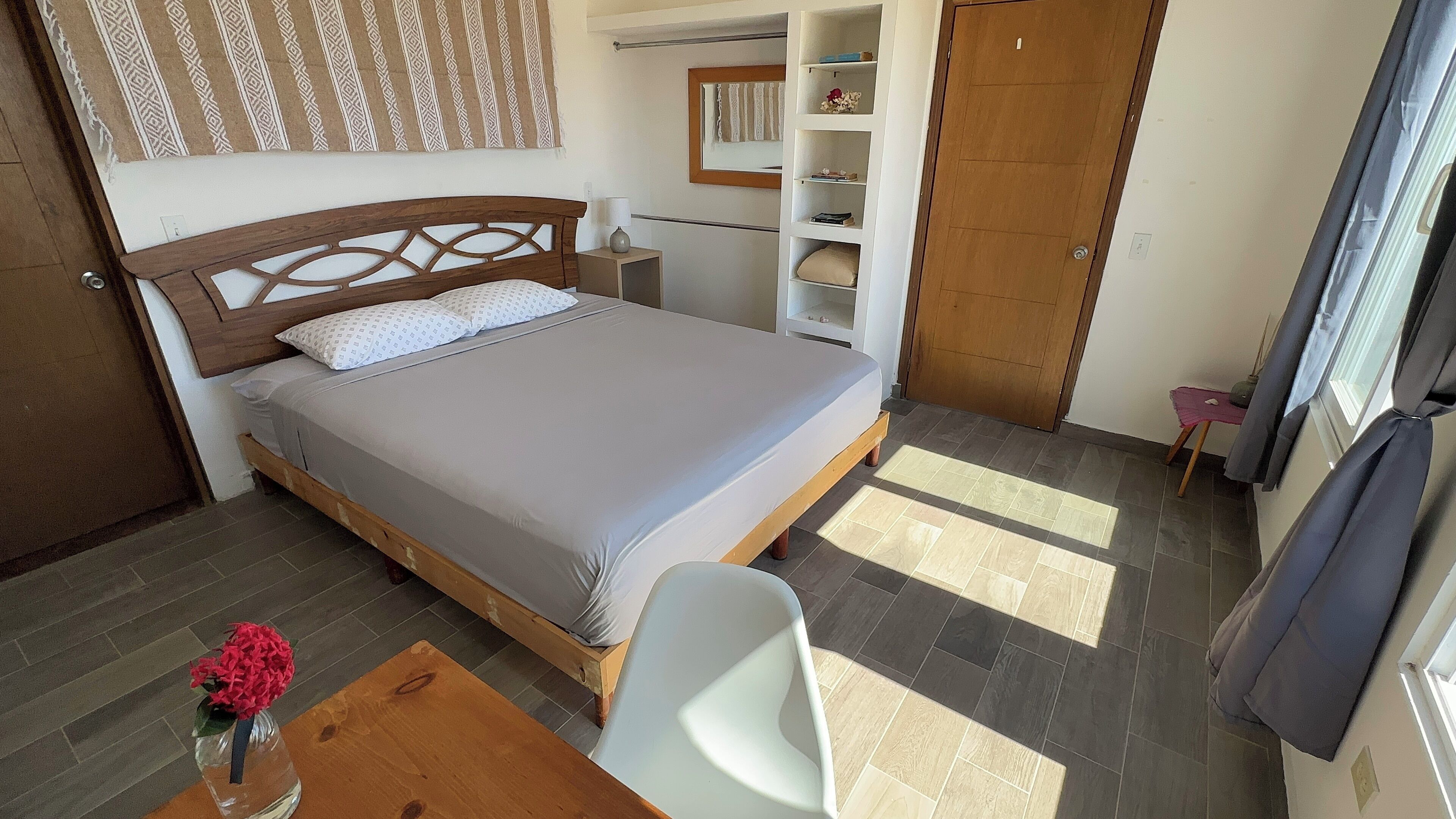 Een netjes ingerichte slaapkamer met een bed, nachtkastje en een klein tafeltje met een bloevas.