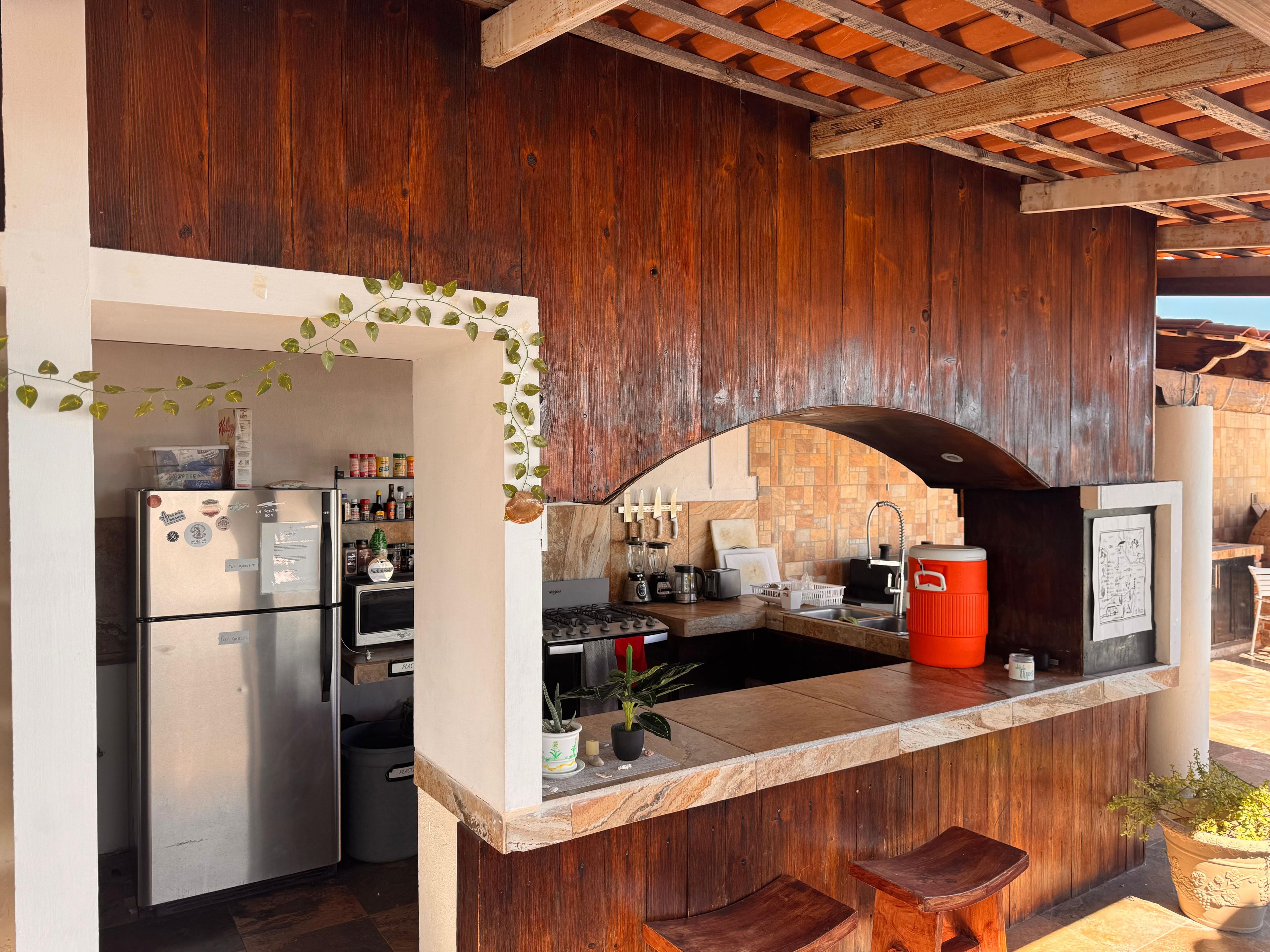 A kitchen with a refrigerator, stove, and sink, featuring wooden walls and a tiled backsplash.