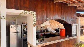 A kitchen with a refrigerator, stove, and sink, featuring wooden walls and a tiled backsplash.