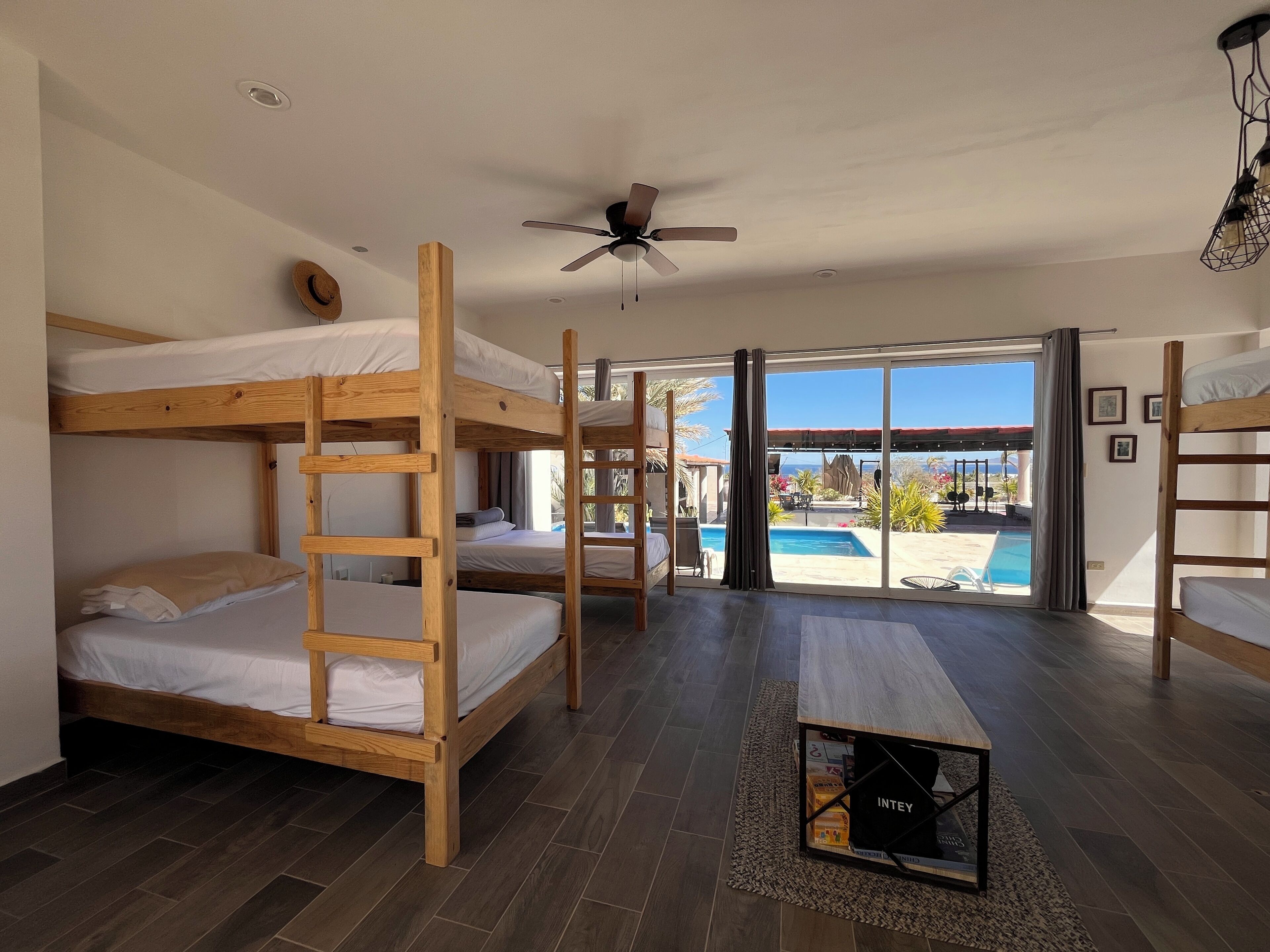 Une chambre avec des lits superposés en bois, un ventilateur de plafond et une vue sur une piscine extérieure.