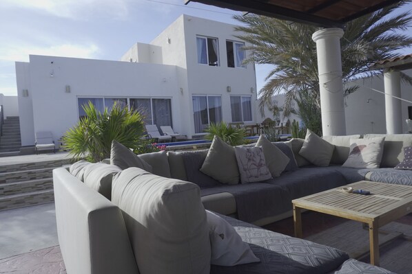 A modern outdoor seating area with a sofa, cushions, and a wooden table. - The Colony La Ventana (La Ventana)