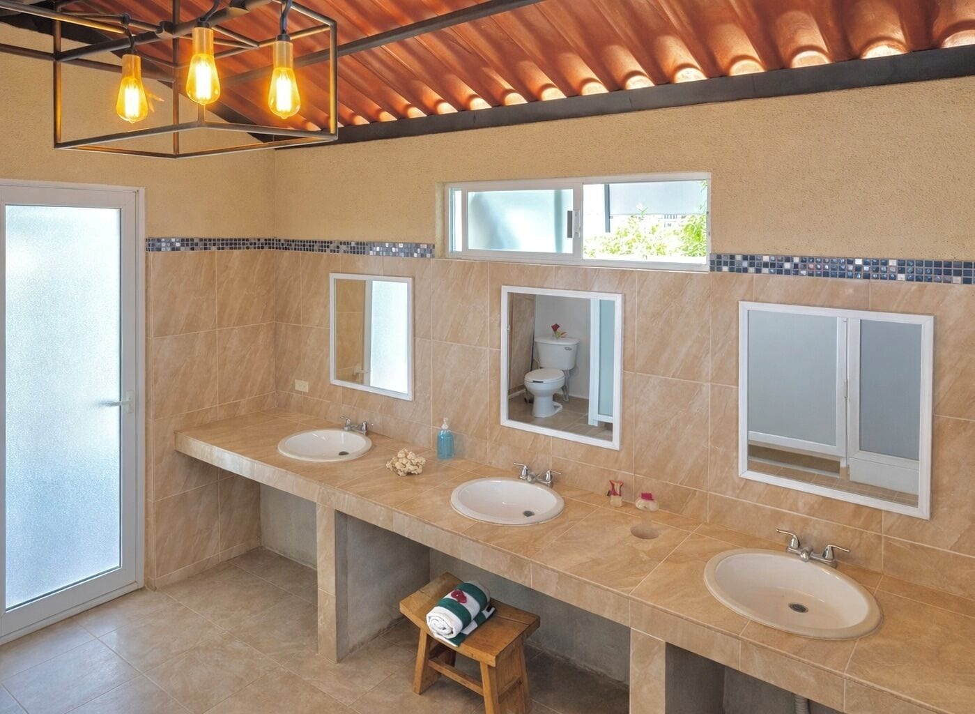 A modern bathroom with three sinks, a shower, and a toilet. There are mirrors above each sink and a window above the toilet.
