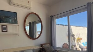 A room with a wooden desk, a chair, a small table with a vase, a mirror, and a window with a view of the outside. - The Colony La Ventana (La Ventana)