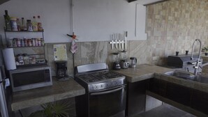 A compact kitchen with a gas stove, oven, microwave, and a sink. There are shelves with various kitchen items and a potted plant. - The Colony La Ventana (La Ventana)