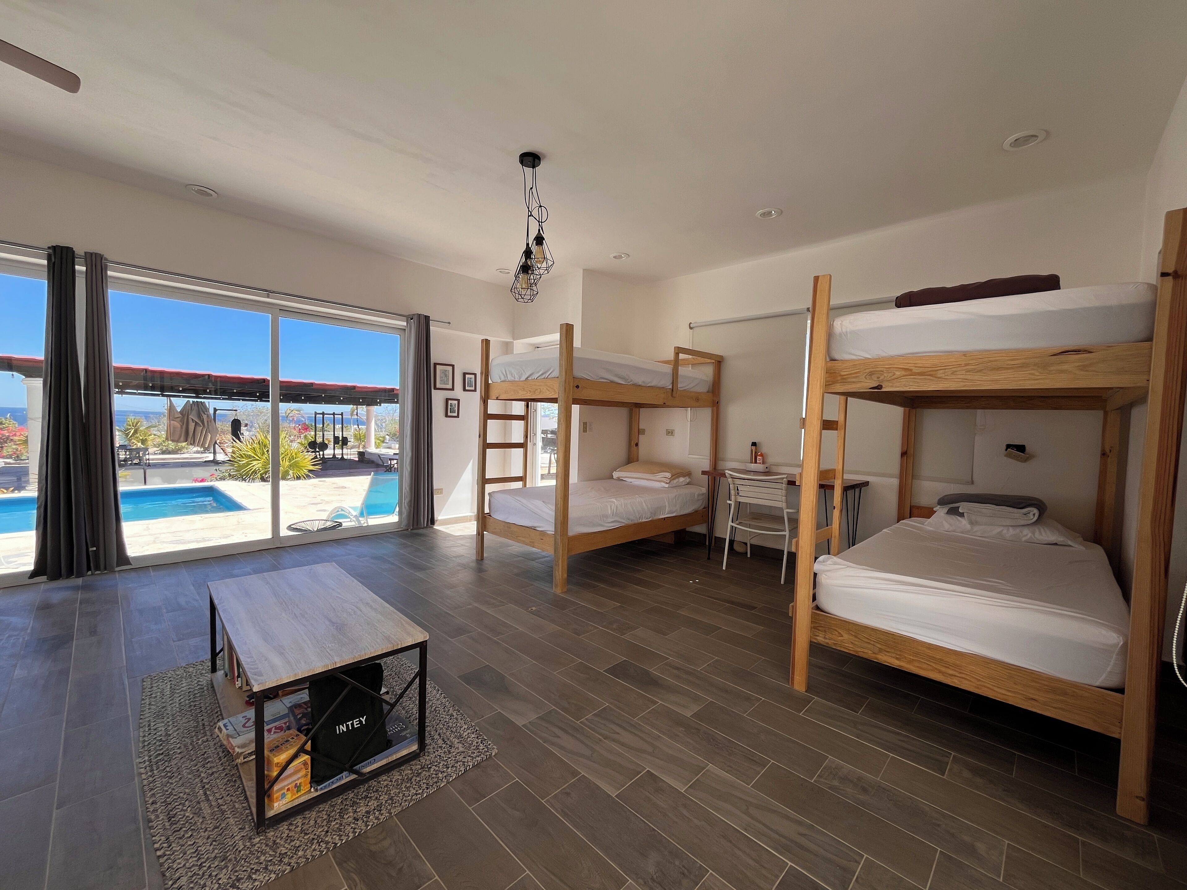 Ein Zimmer mit drei Etagenbetten, einem kleinen Schreibtisch und einem großen Fenster mit Blick auf einen Pool.