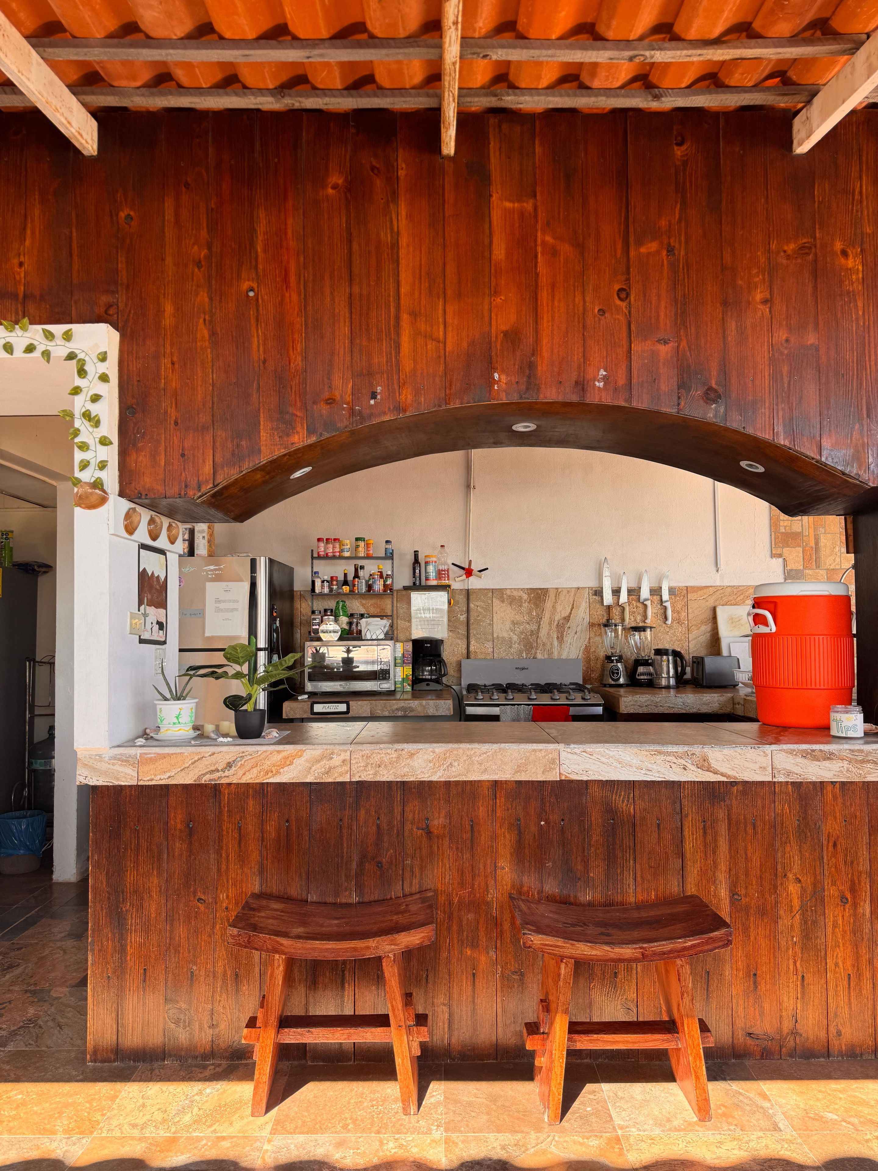 A rustic kitchen with wooden cabinets, a marble countertop, and a red cooler.