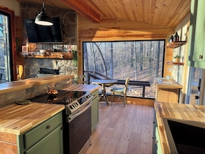Eine moderne Küche mit Steinwand, Holzboden und großen Fenstern mit Blick auf einen Wald.
