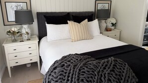 A neatly arranged bedroom with a large bed, two bedside tables, a nightstand, and a decorative vase with flowers.