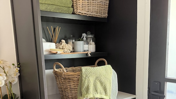 A laundry area with a washing machine, wicker baskets, and shelves with storage items.