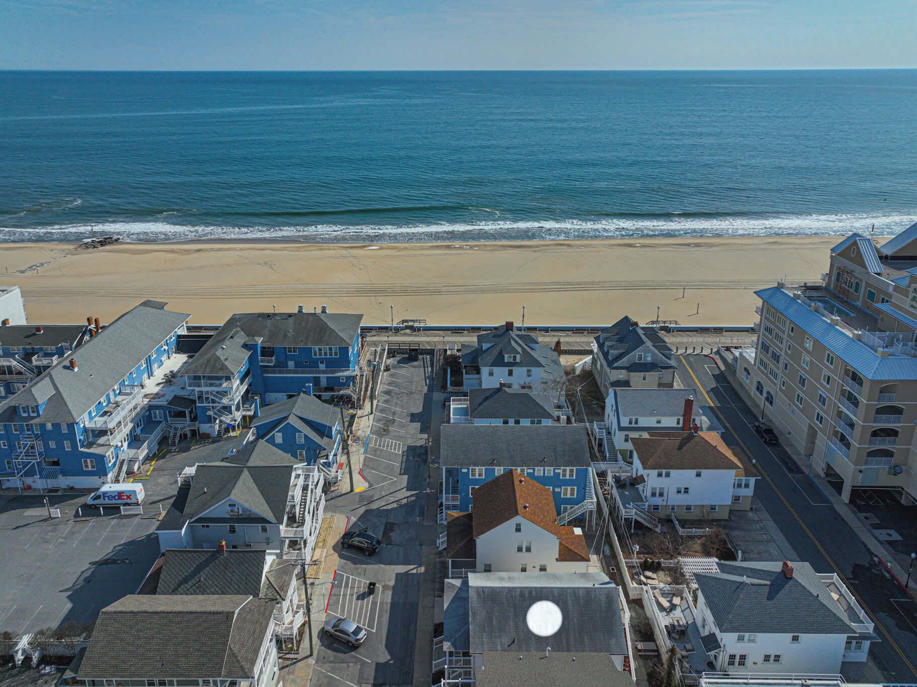 A coastal hotel with multiple buildings, a parking lot, and a beach view.