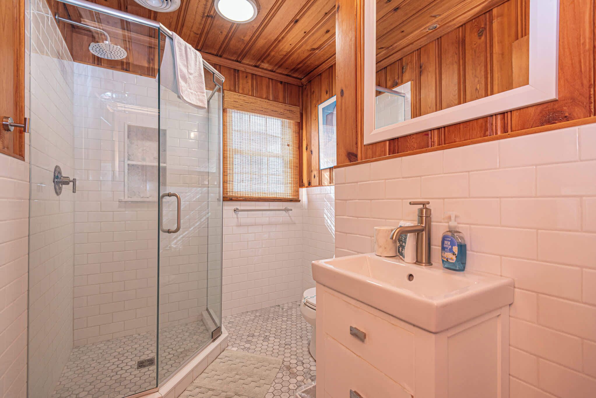 Une salle de bain avec une douche à parois de verre, un lavabo blanc et un meuble-lavabo en bois.