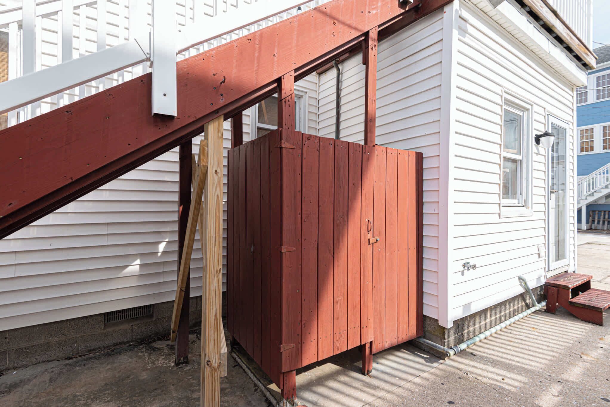 Une clôture en bois rouge est adossée à une maison blanche qui possède une fenêtre et une porte.