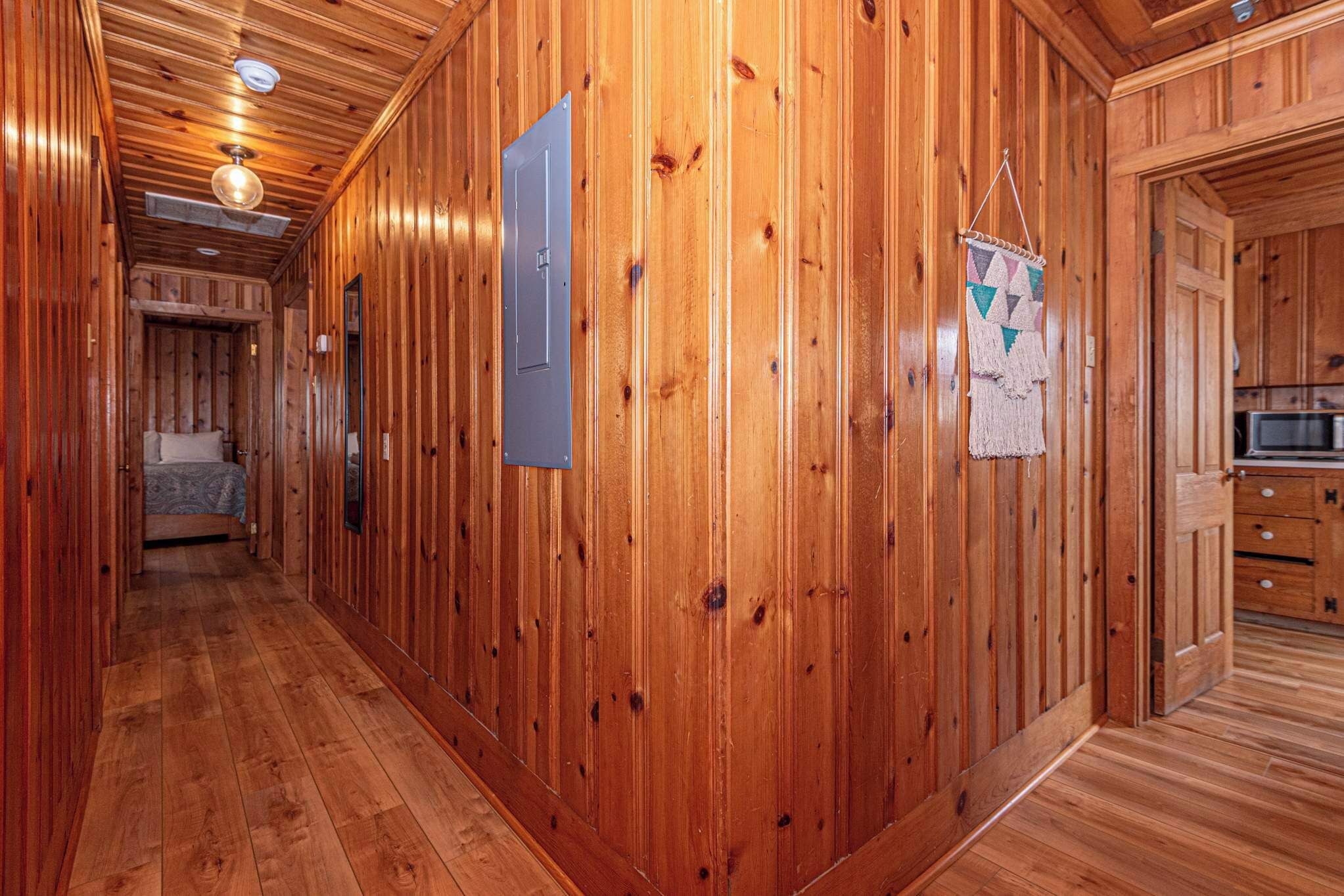 Interior de una cabaña de madera con un pasillo que conduce a un dormitorio y una zona de cocina.