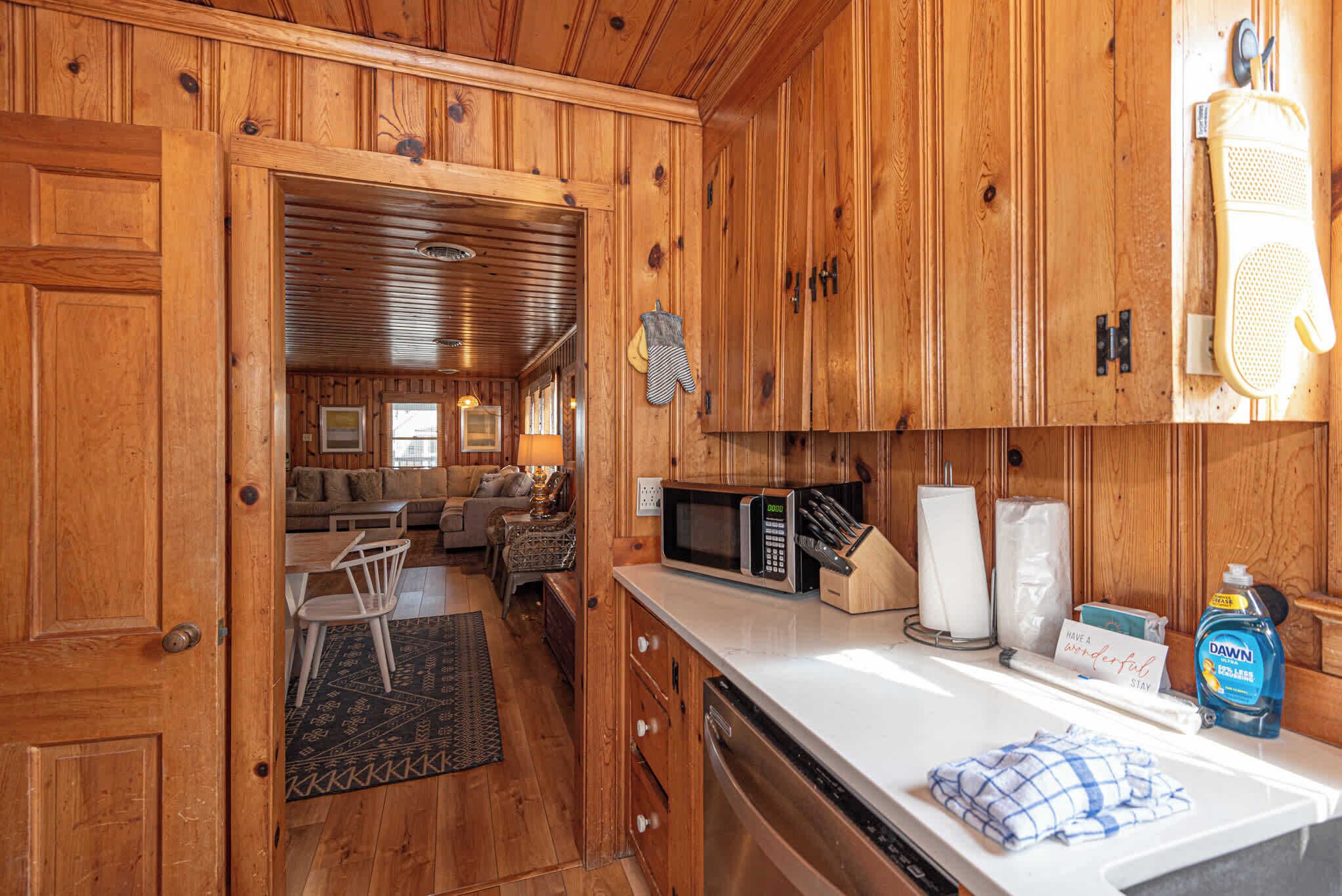 A wooden cabin interior with a kitchen area featuring a microwave, a sink, and a dish soap bottle.