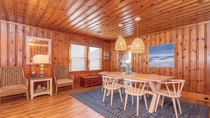 Una habitación con paneles de madera, una mesa de comedor, sillas, un tapete estampado y un ventanal grande.