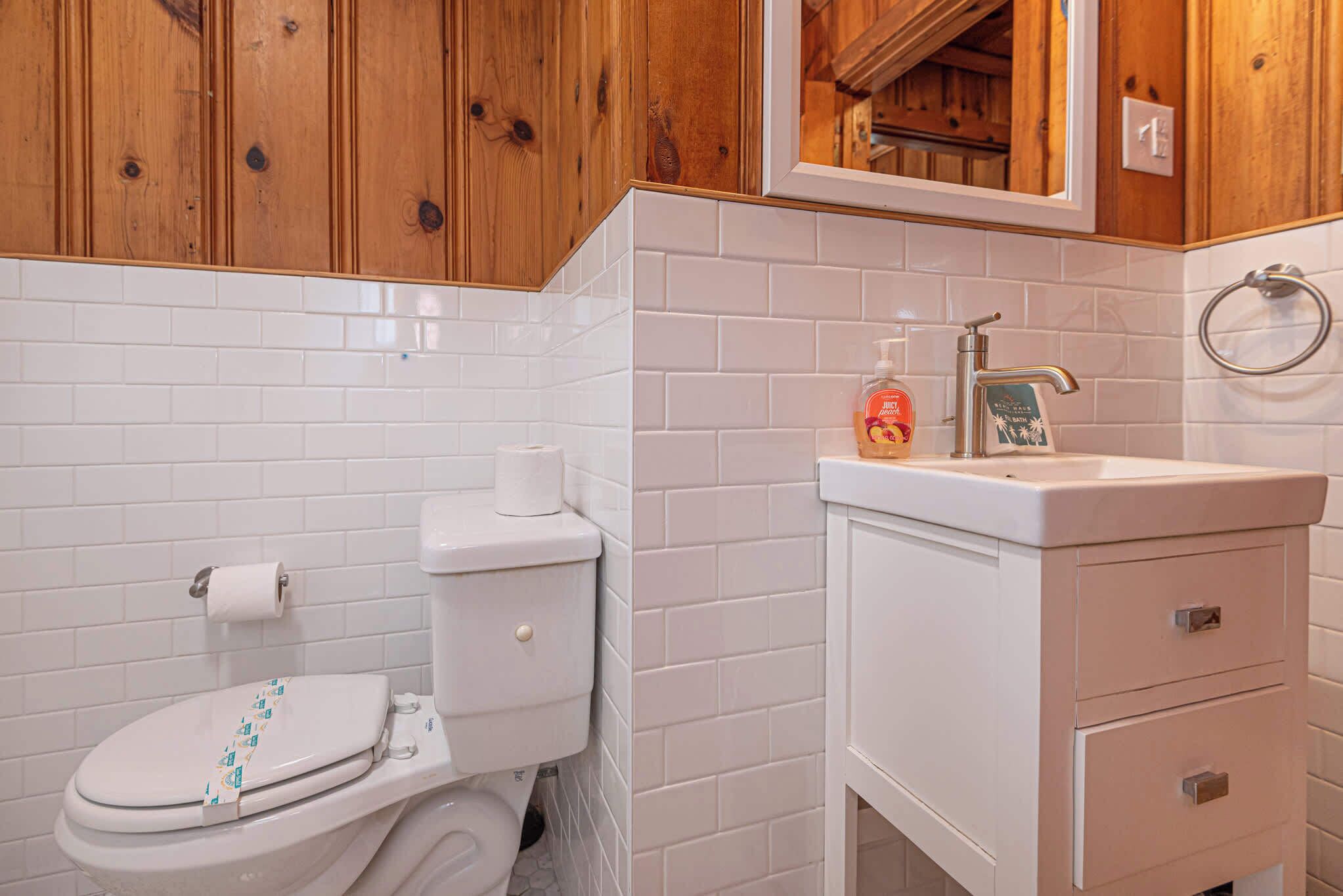 Un baño con inodoro blanco, lavamanos con dispensador de jabón y armarios de madera.