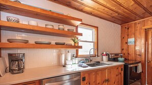 Una cocina con armarios de madera, lavavajillas de acero inoxidable, cafetera y una ventana sobre el fregadero.