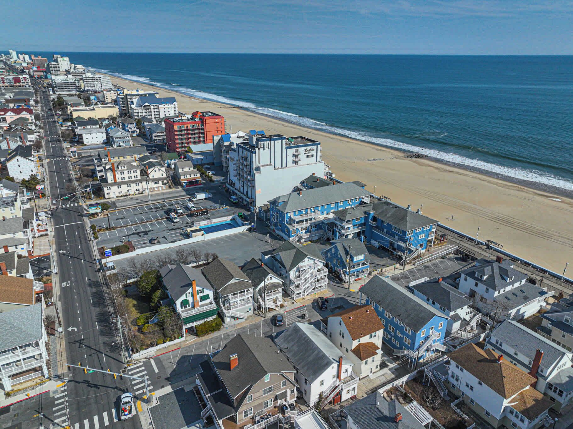 Luchtbeeld van een kustplaatsje met een strand, gebouwen en een opvallend hotel met een blauwe gevel.