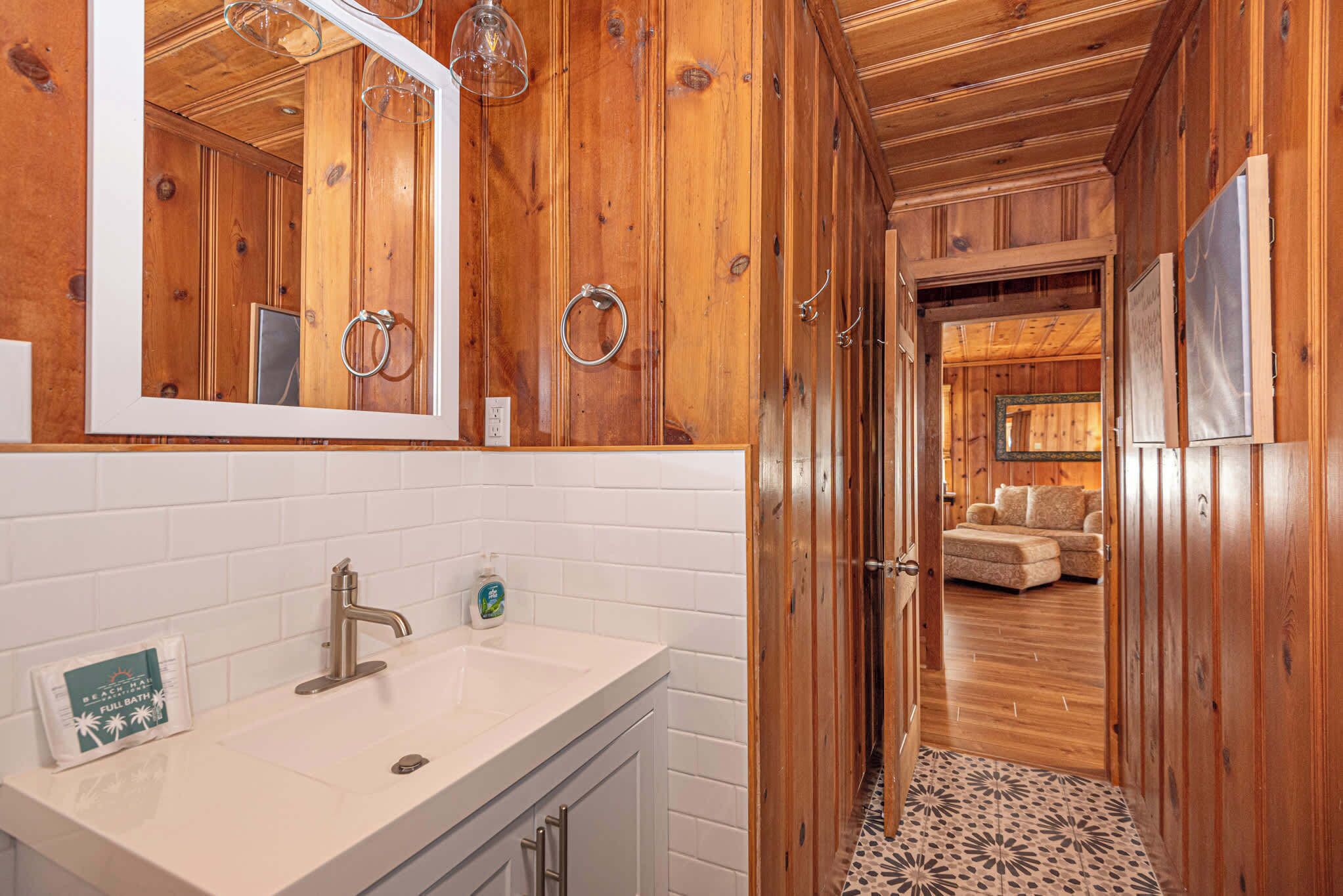 Ein Holzinterieur mit einem Badezimmer, das ein weißes Waschbecken, einen Spiegel und einen Seifenspender zeigt.