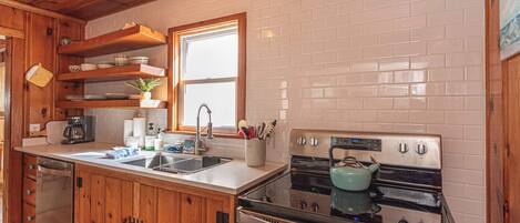 A kitchen with wooden cabinets, a stainless steel dishwasher, a double sink, a stove, and a window with natural light.